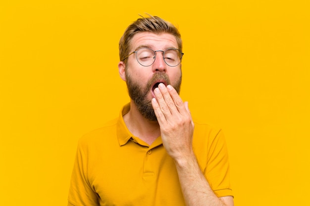 Young blonde man yawning lazily early in the morning