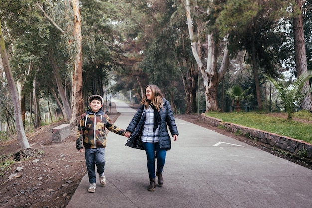 Young blonde mother walking and talking with her young son in a park road Single parent family