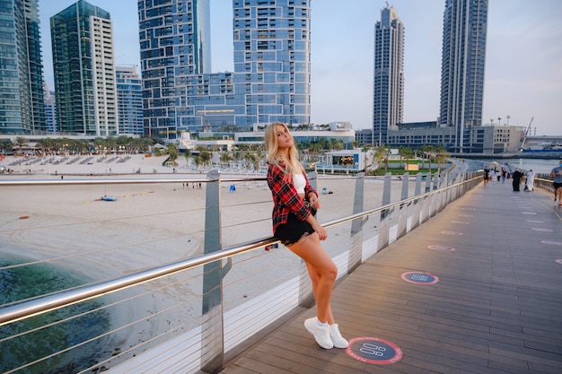 Young blonde travel woman walking on the street outdoors in Dubai city. Dubai marina in United Arab Emirates. UAE summer destination.