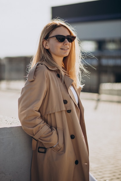 Young blonde woman in beige coat walking in the street