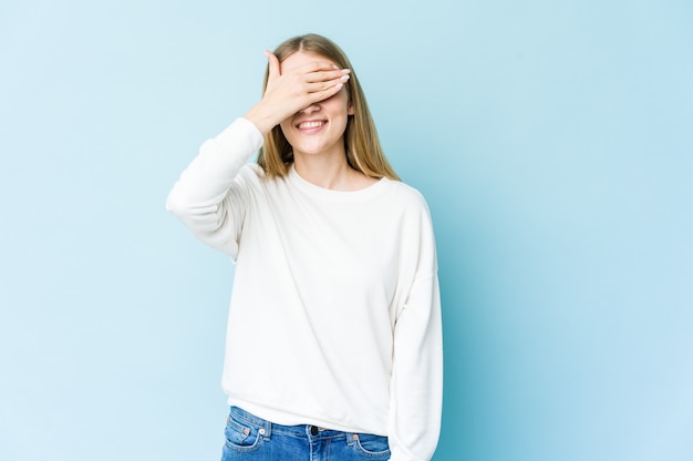 Young blonde woman covers eyes with hands, smiles broadly waiting for a surprise.