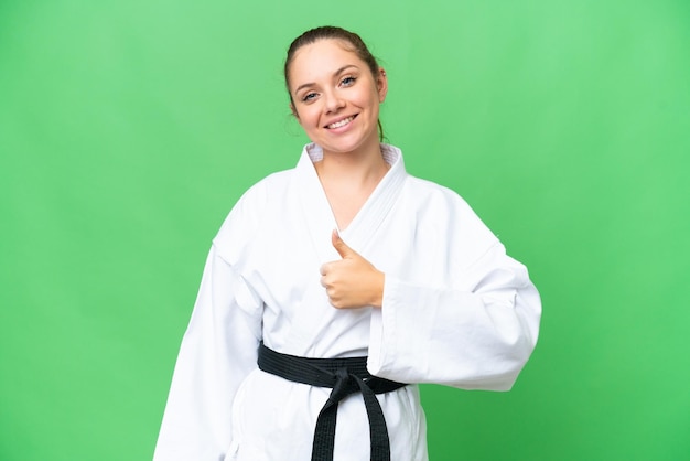 Young blonde woman doing karate over isolated chroma key background giving a thumbs up gesture