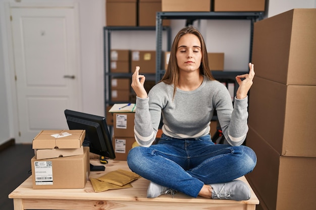 Young blonde woman ecommerce business worker doing yoga sitting on table at office