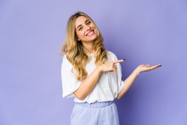 Young blonde woman excited pointing to side