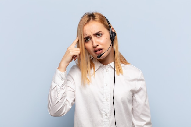 Young blonde woman feeling confused and puzzled, showing you are insane, crazy or out of your mind