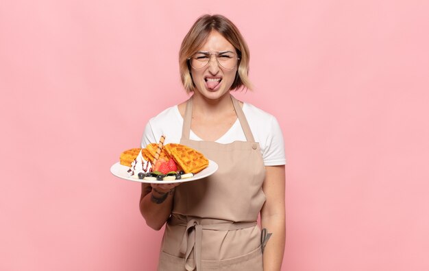 Young blonde woman feeling disgusted and irritated, sticking tongue out, disliking something nasty and yucky