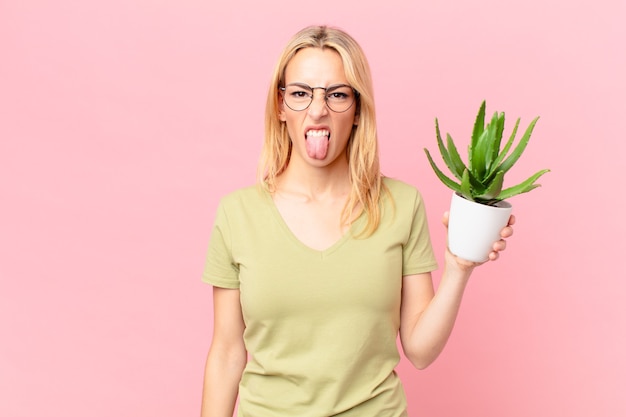 Photo young blonde woman feeling disgusted and irritated and tongue out and holding a cactus