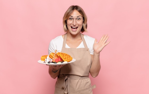 Young blonde woman feeling happy, excited, surprised or shocked, smiling and astonished at something unbelievable