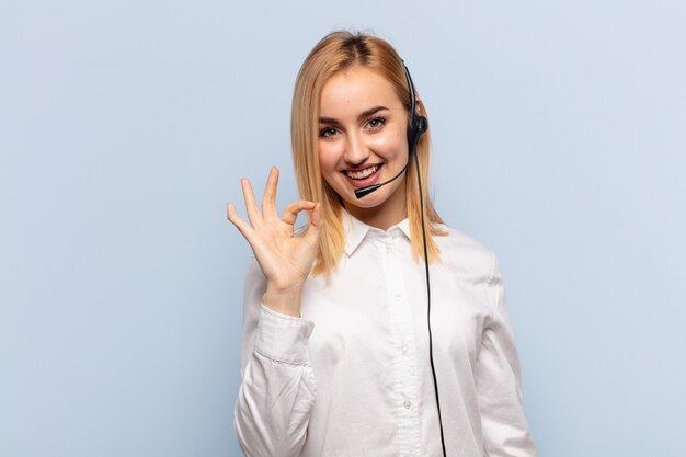 Young blonde woman feeling happy, relaxed and satisfied, showing approval with okay gesture, smiling