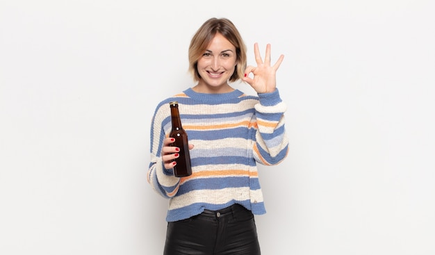 Young blonde woman feeling happy, relaxed and satisfied, showing approval with okay gesture, smiling