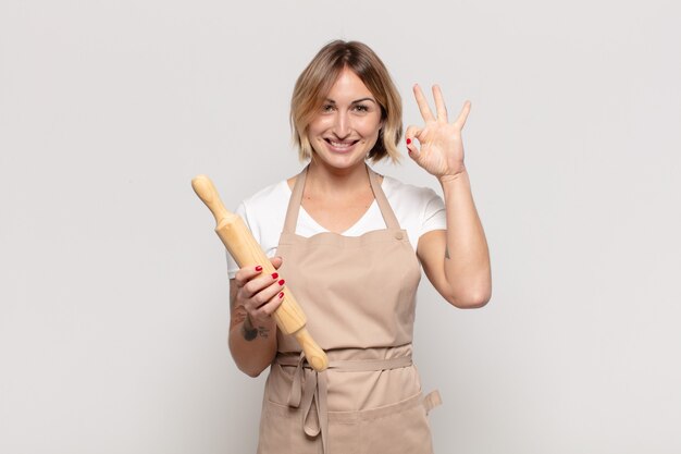 Young blonde woman feeling happy, relaxed and satisfied, showing approval with okay gesture, smiling