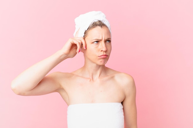 Young blonde woman feeling puzzled and confused, scratching head and after shower