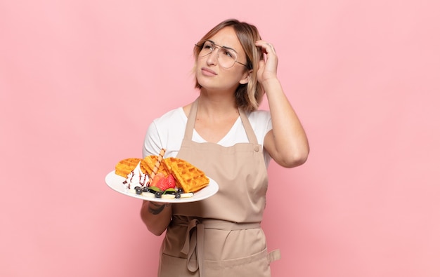 Young blonde woman feeling puzzled and confused, scratching head and looking to the side