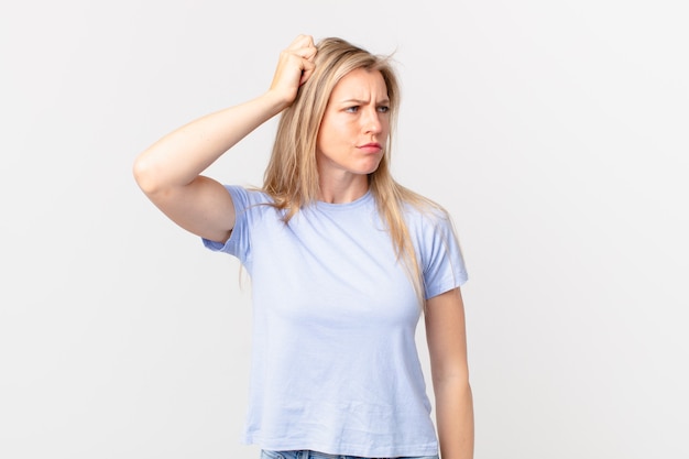 Young blonde woman feeling puzzled and confused, scratching head