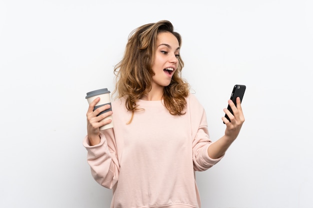 Young blonde woman holding coffee to take away and a mobile