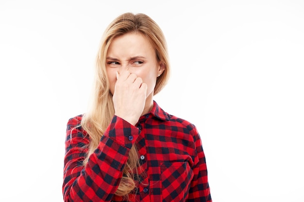 Young blonde woman holding nose to avoid disgusted smell pinches nose and mouth with fingers and holding breath isolated on white background