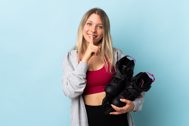 Young blonde woman holding a roller skates isolated on pink wall doing silence gesture