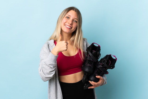 Young blonde woman holding a roller skates isolated on pink wall giving a thumbs up gesture