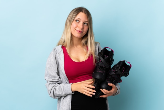 Young blonde woman holding a roller skates isolated on pink wall standing and looking to the side