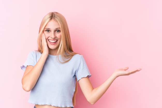 Young blonde woman holds something on a palm, keep hand over cheek