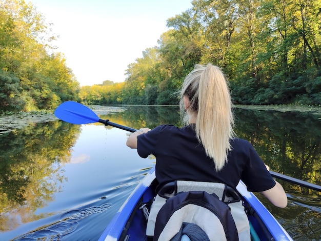 A young blonde woman is rowing a kayak on the river Rear view Active recreation and tourism