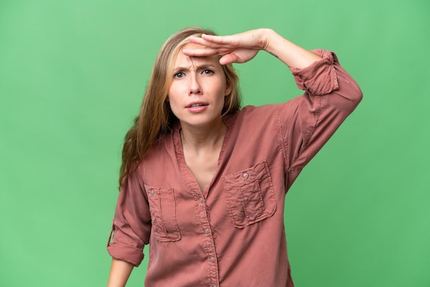 Young blonde woman over isolated background looking far away with hand to look something