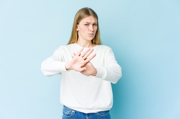 Young blonde woman isolated on blue wall doing a denial gesture