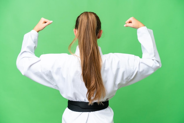 Young blonde woman over isolated chroma key background doing karate in back position