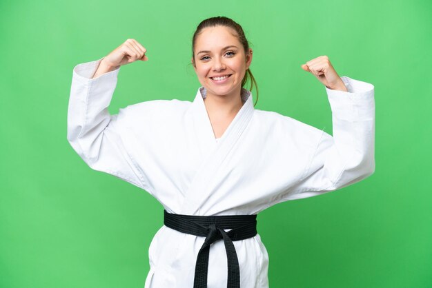 Young blonde woman over isolated chroma key background doing karate and making strong gesture