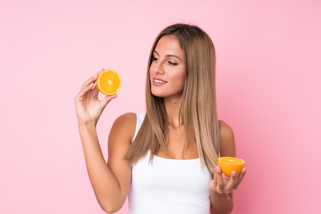 Young blonde woman over isolated  holding an orange