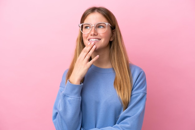 Young blonde woman isolated on pink background With glasses and thinking while looking up