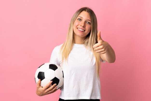 Young blonde woman isolated on pink wall with soccer ball and with thumb up