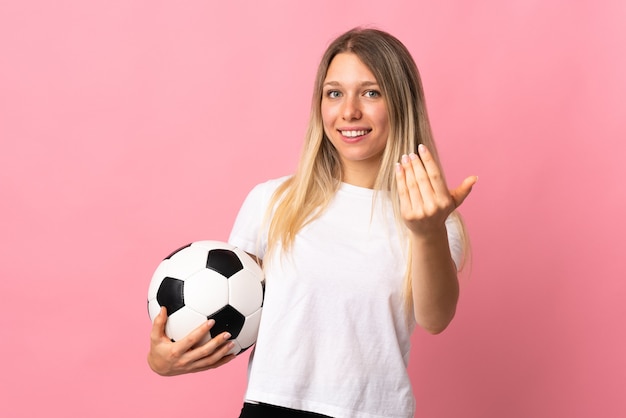 Young blonde woman isolated on pink with soccer ball and doing coming gesture