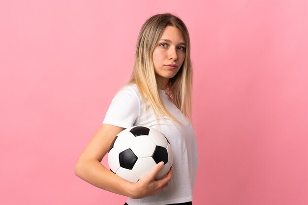 Young blonde woman isolated on pink with soccer ball