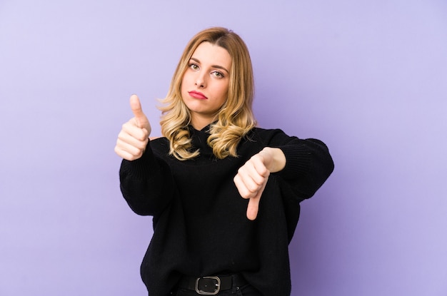 Young blonde woman isolated showing thumbs up and thumbs down, difficult choose concept