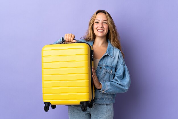 Young blonde woman isolated in vacation with travel suitcase