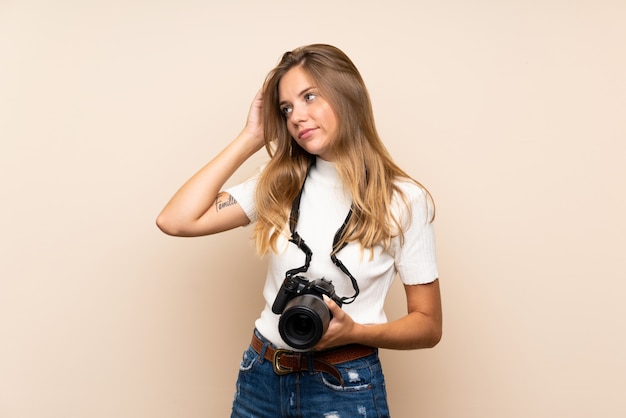 Photo young blonde woman over isolated wall with a professional camera and thinking