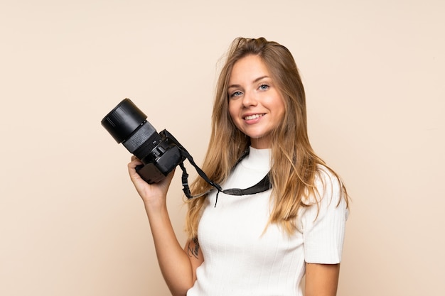 Photo young blonde woman over isolated wall with a professional camera