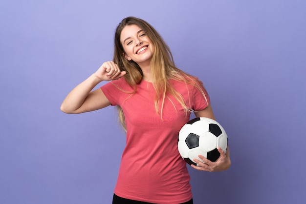 Young blonde woman over isolated wall with soccer ball and proud of himself