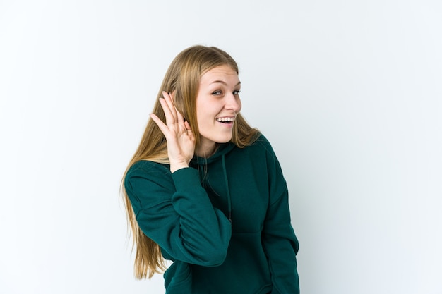 Young blonde woman isolated on white wall trying to listening a gossip.