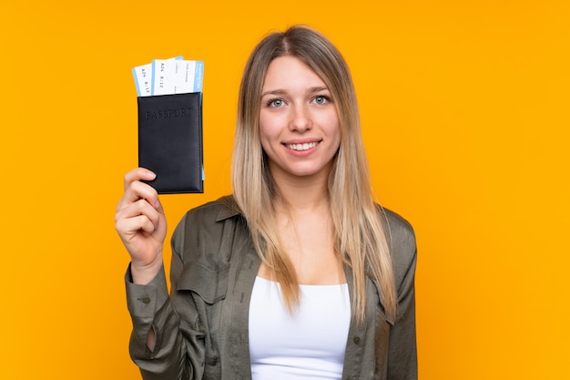 Young blonde woman over isolated yellow wall happy in vacation with passport and plane tickets