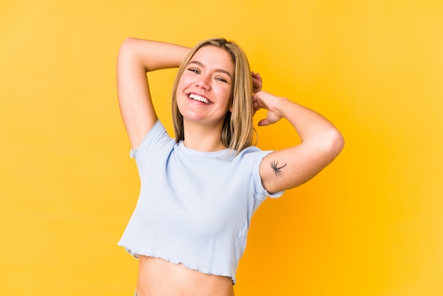 Young blonde woman isolated on yellow wall stretching arms, relaxed position