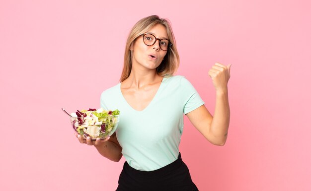 Young blonde woman looking astonished in disbelief and holding a salad