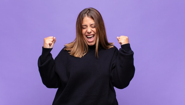 Young blonde woman looking extremely happy and surprised, celebrating success, shouting and jumping