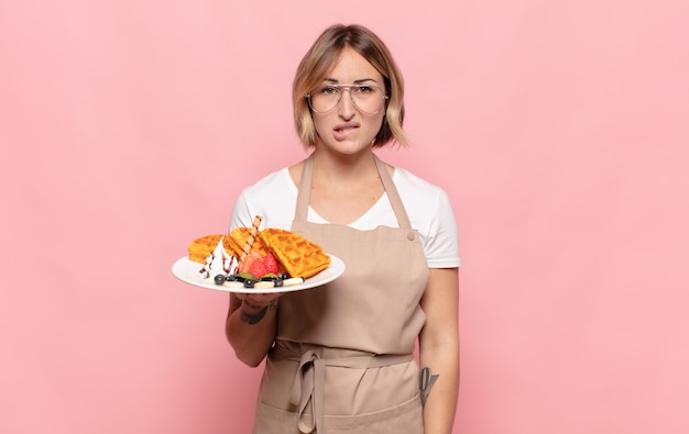 Young blonde woman looking puzzled and confused, biting lip with a nervous gesture, not knowing the answer to the problem