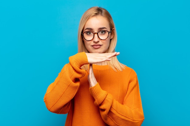 Young blonde woman looking serious, stern, angry and displeased, making time out sign