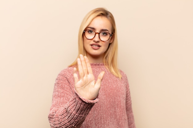 Young blonde woman looking serious, stern, displeased and angry showing open palm making stop gesture