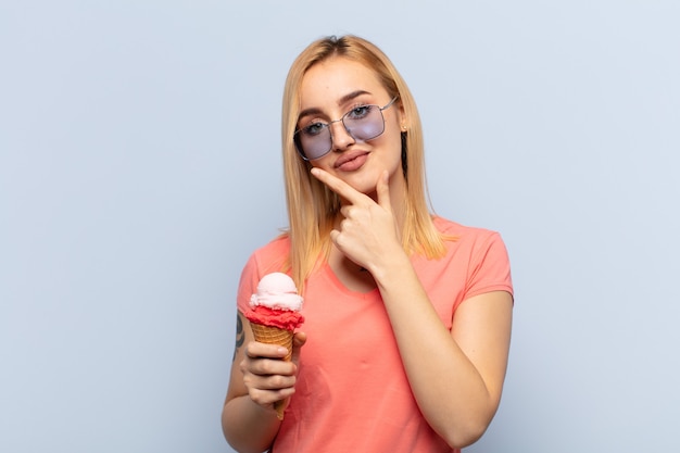 Young blonde woman looking serious, thoughtful and distrustful, with one arm crossed and hand on chin, weighting options