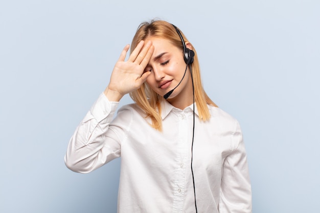 Young blonde woman looking stressed, tired and frustrated, drying sweat off forehead, feeling hopeless and exhausted