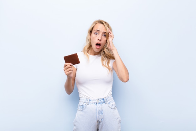 Young blonde woman looking surprised, open-mouthed, shocked, realizing a new thought, idea or concept holding a wallet